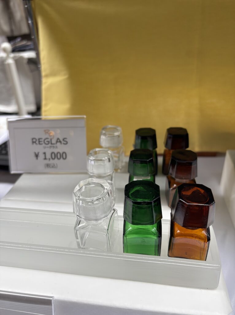 REGLASの角フタ薬瓶をイベント販売ブースにディスプレイした様子。クリア、グリーン、ブラウンの3色展開で、価格は税込1,000円。